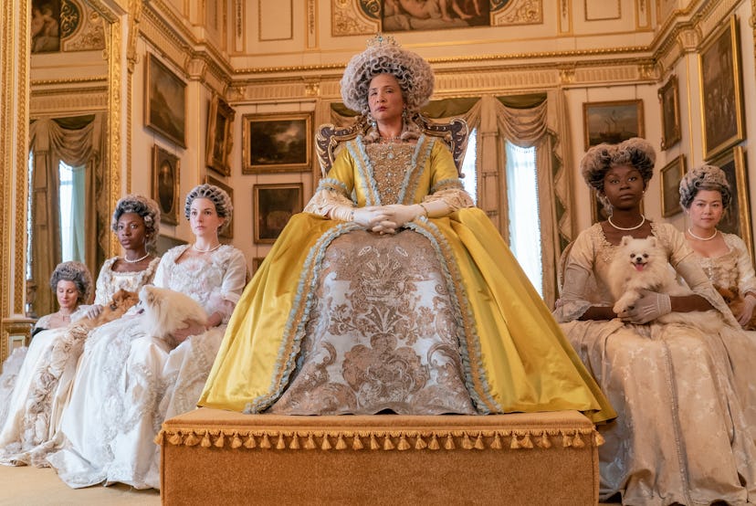 Queen Charlotte sitting on a throne in a yellow dress with a large hoop skirt.