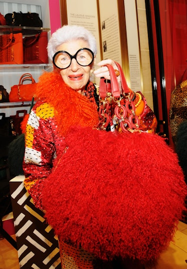 Iris Apfel holding up a giant puffball-shaped handbag