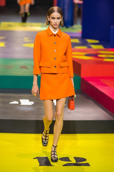 A model walking on the runway in an orange jacket and skirt by Dior