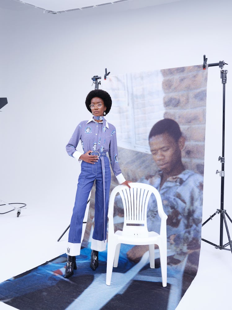 A model posing in a blue shirt and blue denim jeans by Thebe Magugu in a studio