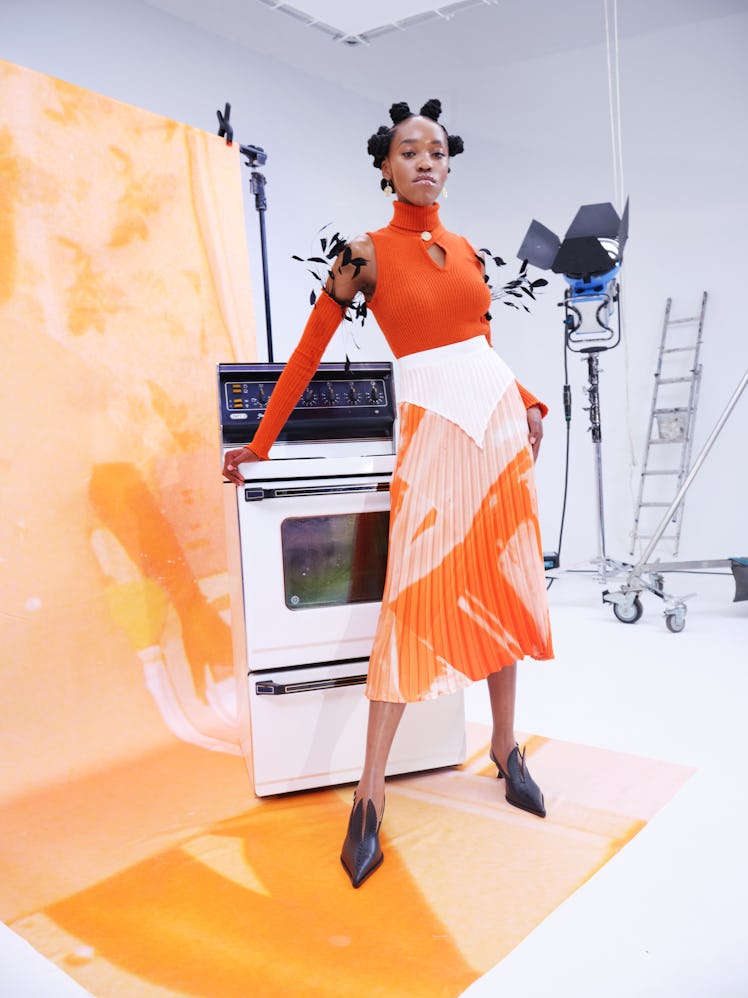 A model posing in an orange-white dress by Thebe Magugu in a studio
