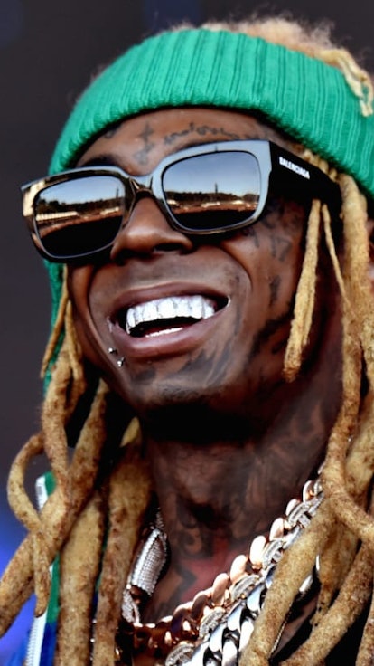 Lil Wayne in a green headband, black sunglasses and a green and purple jacket, smiling