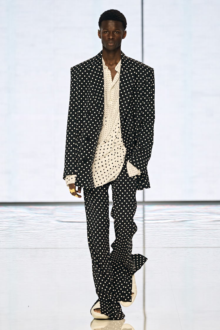 A model walking on a runway in a black polka dot suit and shirt by Balmain