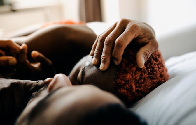 Two men embracing while laying in bed together.