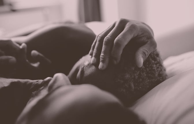 Two men embracing while laying in bed together.