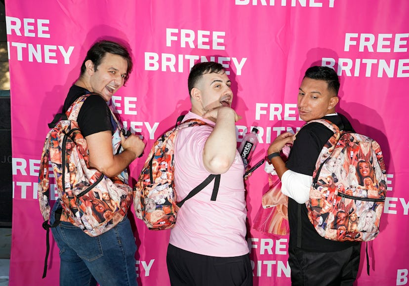 Fans with Britney Spears backpacks posing in front of a pink background that says "Free Britney" all...