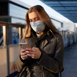 Woman in mask at train station looking at her phone.