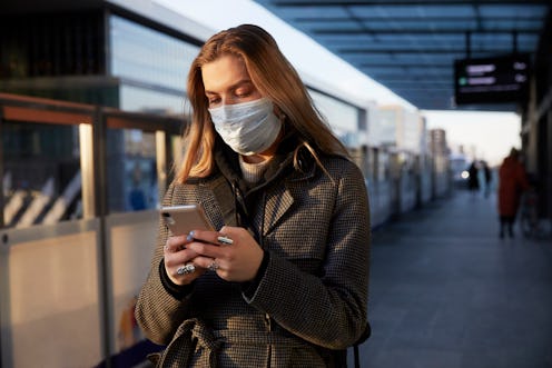 Woman in mask at train station looking at her phone.