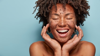 A curly-haired woman smiling with her eyes close while using an Astaxanthin face scrub