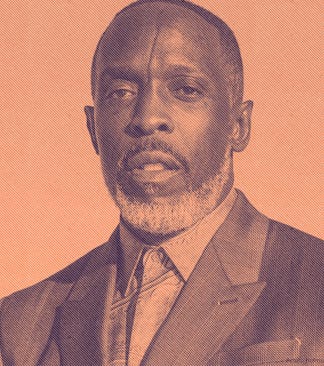 Michael K. Williams posing in a suit, with an orange background. 