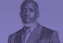 Michael K. Williams posing in a suit, with an orange background. 
