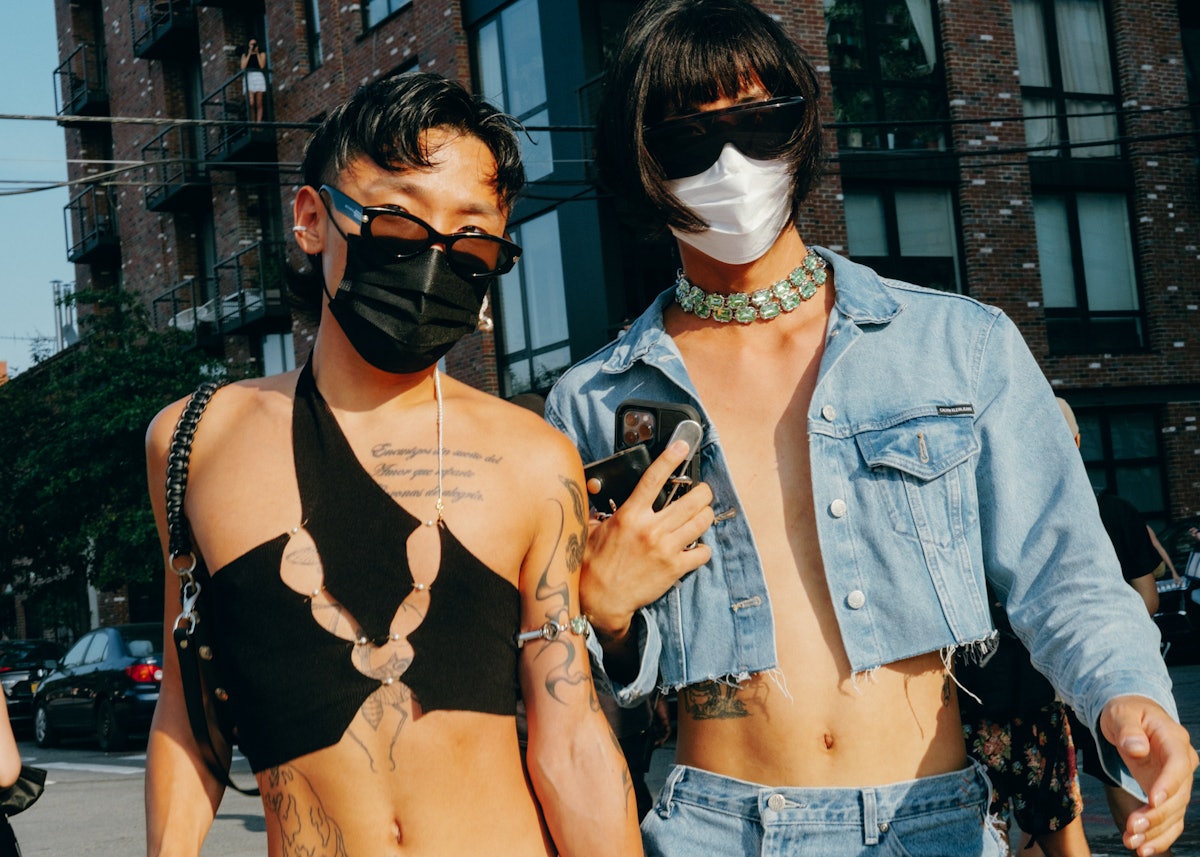 Two friends pose for the photo.  The person on the left is wearing a cropped top.  The person on the right is wearing a crop top denim jacket ...