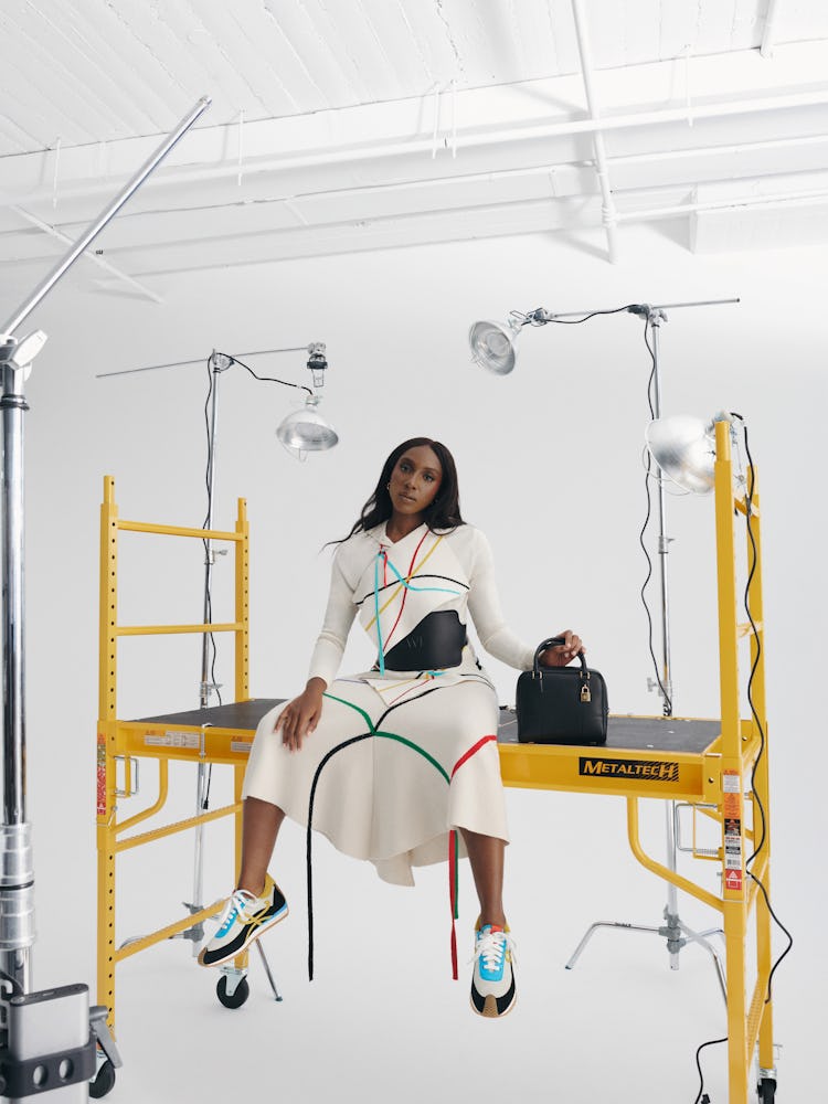 Ziwe posing in a white dress with blue, green, yellow and red stripes and a black bag 