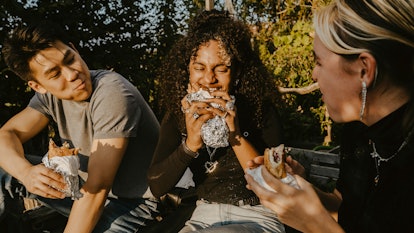 Young woman eating a burrito — one of her favorite foods, per her zodiac sign — with friends.