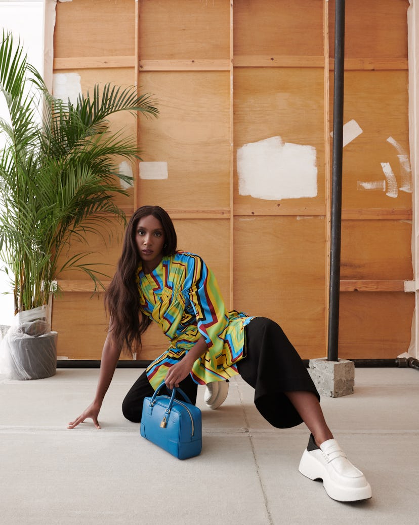 Ziwe Fumudoh crouching on the floor with a Loewe Amazona bag in blue