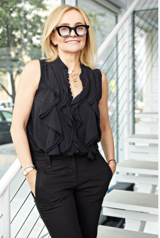 Joanna Czech in a black top and black trousers, and black gasses posing near a staircase