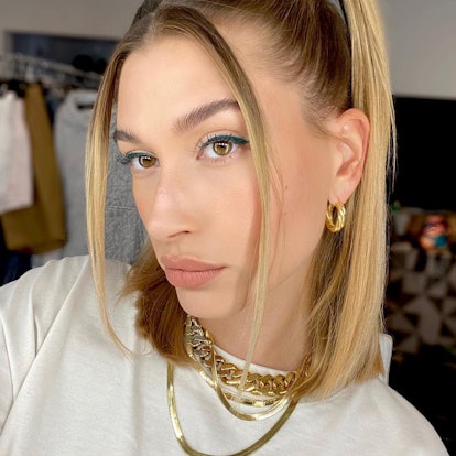 Hailey Bieber wears her hair back, except for two very thin, straight pieces of hair which frame her...