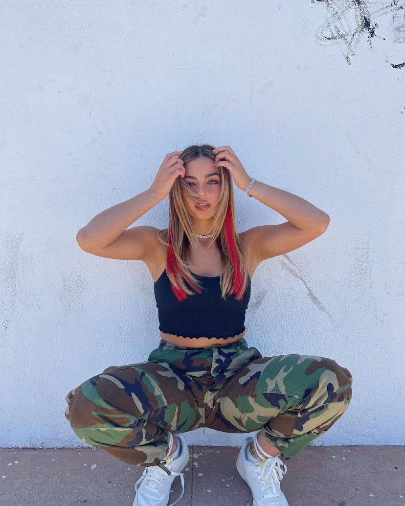 Addison Rae poses with pieces of bright red extensions clipped into her natural hair.