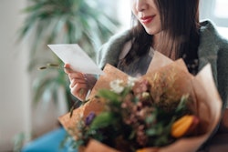 woman holding a bouquet of flowers, reading a handwritten note