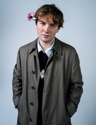 Cooper Hoffman in a brown coat, black sweater, and a shirt, with a flower behind an ear in W Magazin...