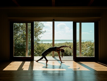 a woman does a stretch in a fitness studio with a tropical view