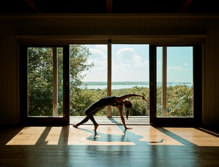 a woman does a stretch in a fitness studio with a tropical view