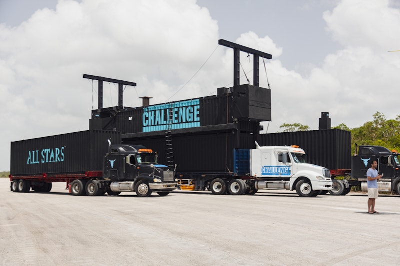 A photo of two semi trucks with black cargo that has blue writing on the side.  One truck says "chal...