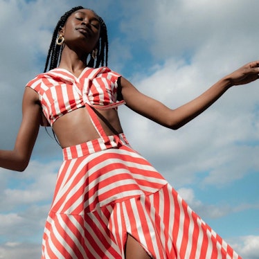 A black model wearing a red and white striped top and skirt set in front of a blue sky with clouds