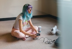A woman with blue hair plays video games while streaming on Twitch. How to use Twitch as a viewer.