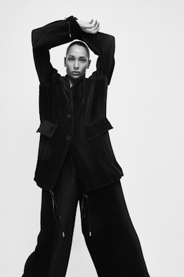 A model posing in a black suit with her arms above her head in black and white
