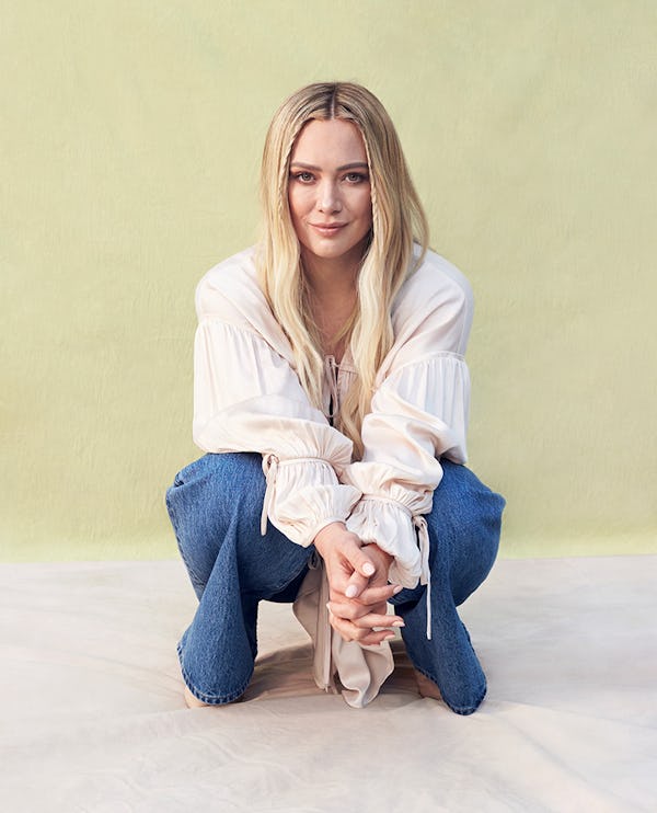 Hilary Duff crouching in a white Tove top, Coach vest and jeans,Astrid & Miyu earrings and Jimmy Cho...