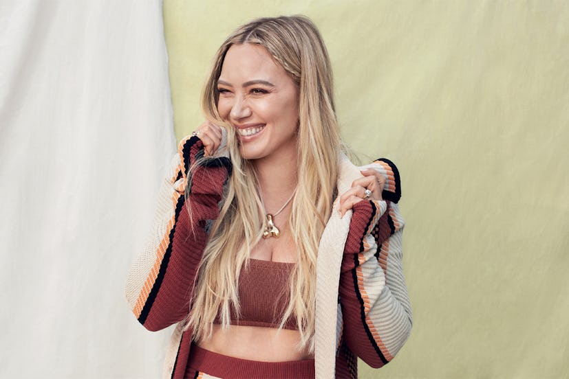 Hillary Duff smiling in a burgundy Tod’s coat, pants and Calle del Mar bandeau