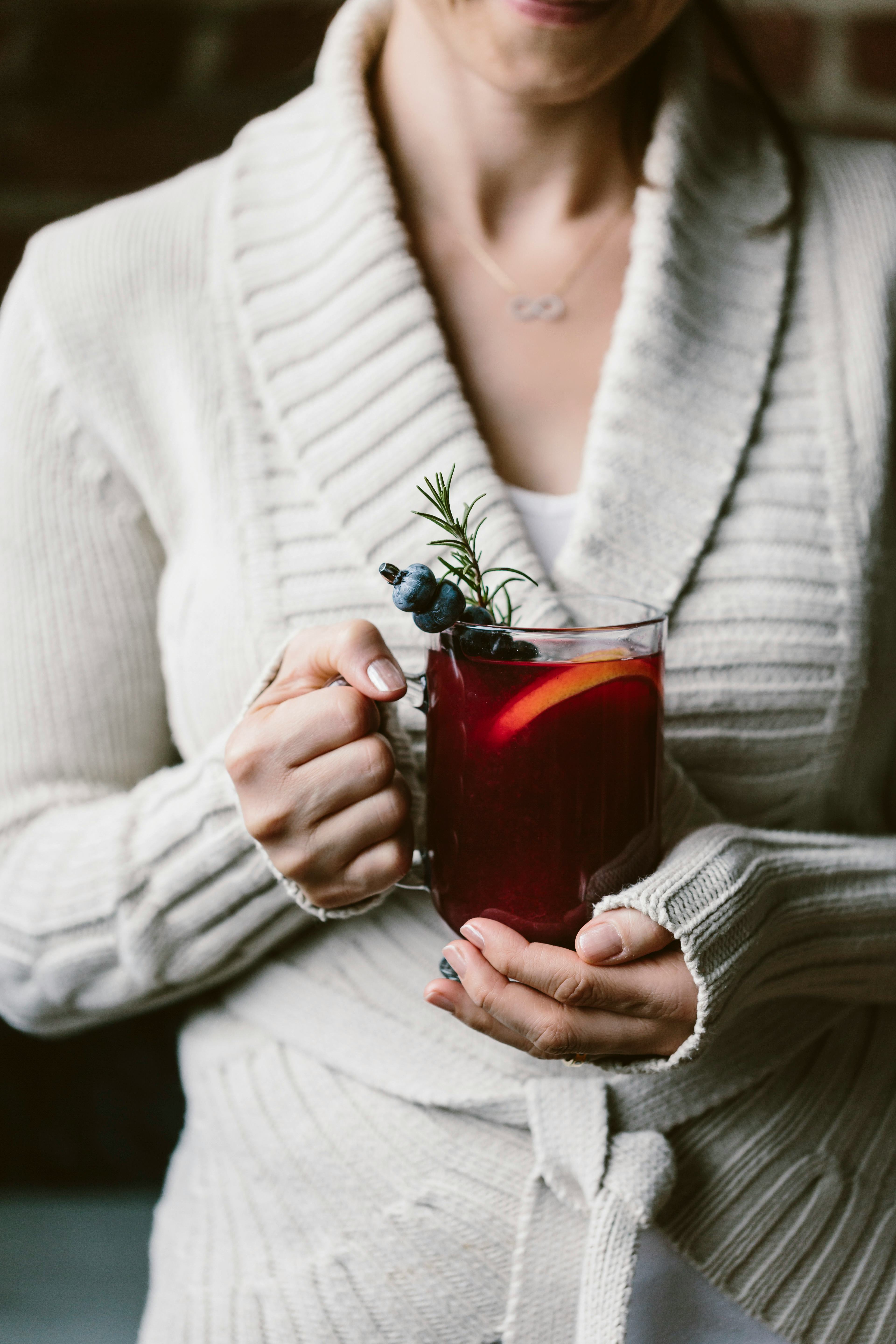 female holding hot toddy warm winter cocktail beverage with blueberry and rosemary garnish