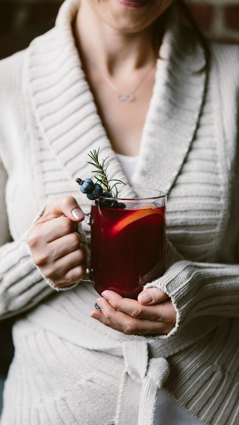 female holding hot toddy warm winter cocktail beverage with blueberry and rosemary garnish