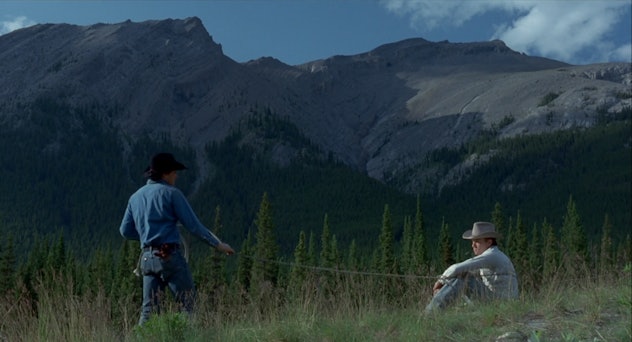 Jack and Ennis stare at each other from across a short distance, mountains behind them.
