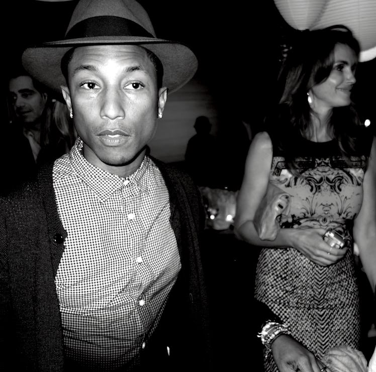 Pharrell Williams in a checkered shirt and fedora hat at a party