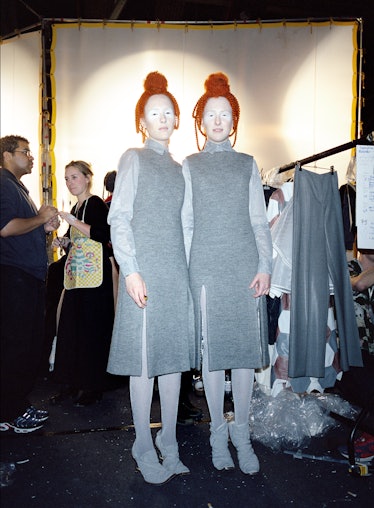 two models wearing grey dresses, heavy makeup and red topknot wigs