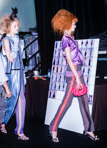 models walk in front of a posterboard featuring different runway looks