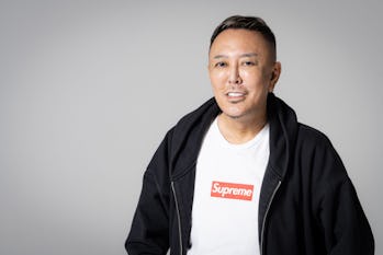 Photo of Nagoshi smiling and wearing a SUPREME red logo white t-shirt with a black zip-up hoodie.