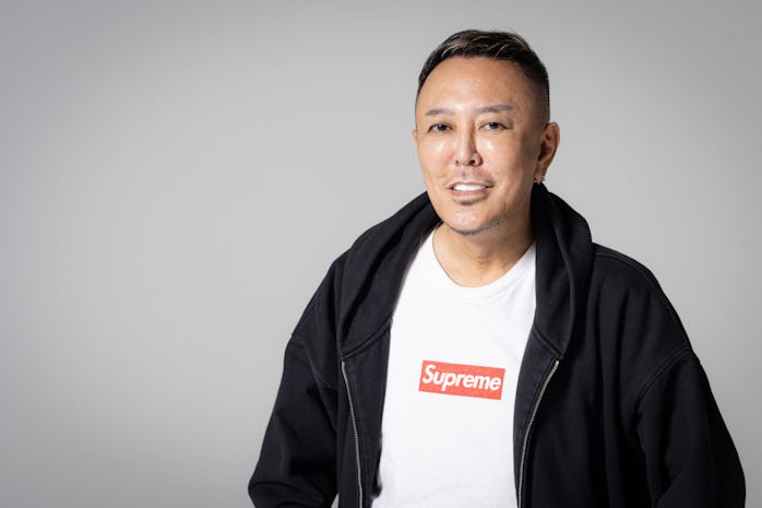 Photo of Nagoshi smiling and wearing a SUPREME red logo white t-shirt with a black zip-up hoodie.