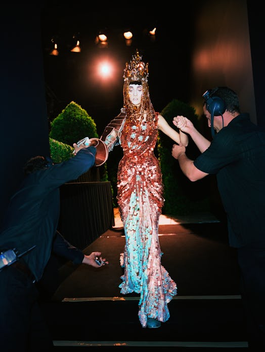 a model on a dark runway wearing a beaded gown and headpiece