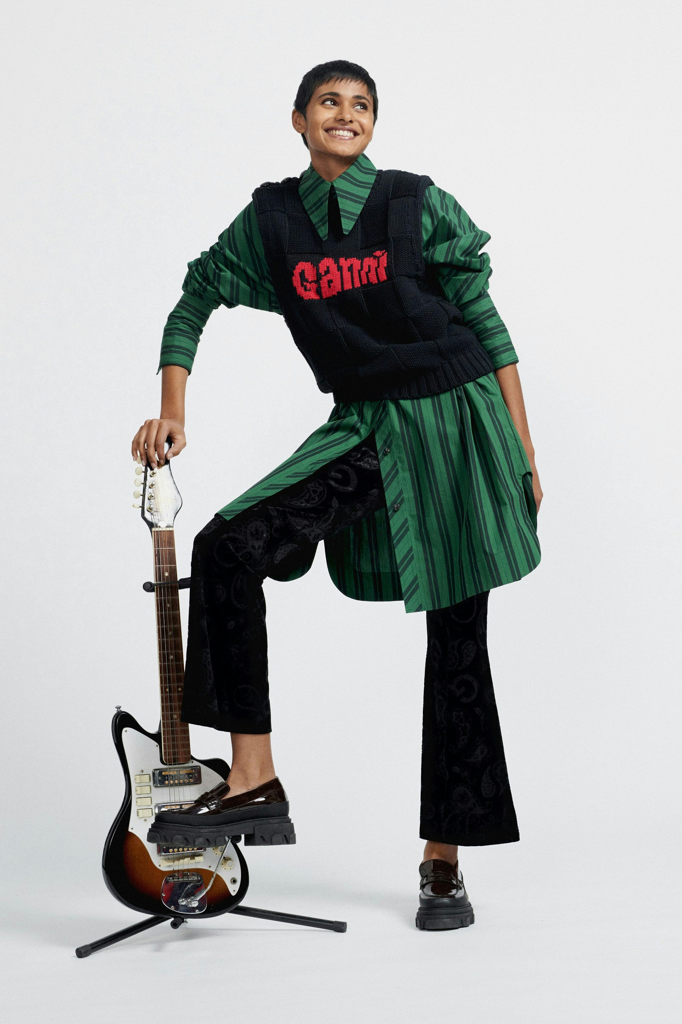 A Ganni model wears an oversized top, sweater vest, flared pants and lug sole loafers.