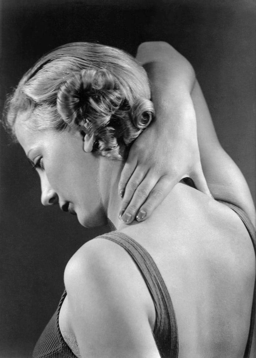 The back of a woman who is holding her hand on her neck in black and white