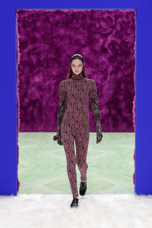 A model walks the runway at Prada in a patterned suit and lace up loafers.