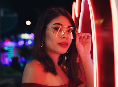 Young woman wearing glasses in red neon lights thinking of how the February 2022 new moon in Aquariu...