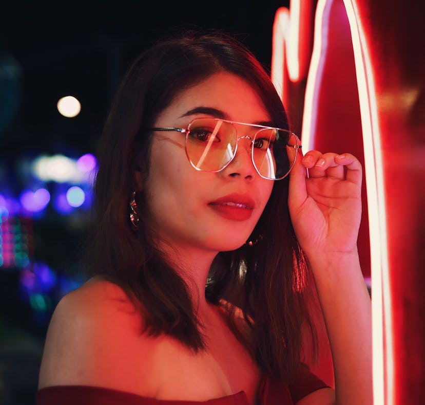 Young woman wearing glasses in red neon lights thinking of how the February 2022 new moon in Aquariu...