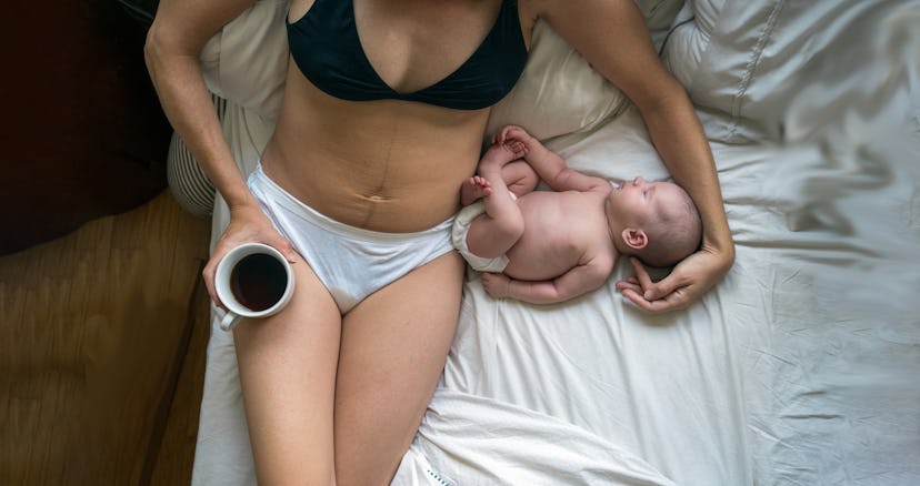 A mom in underwear lying in bed with a cup of coffee with her newborn baby after a C-section with a ...