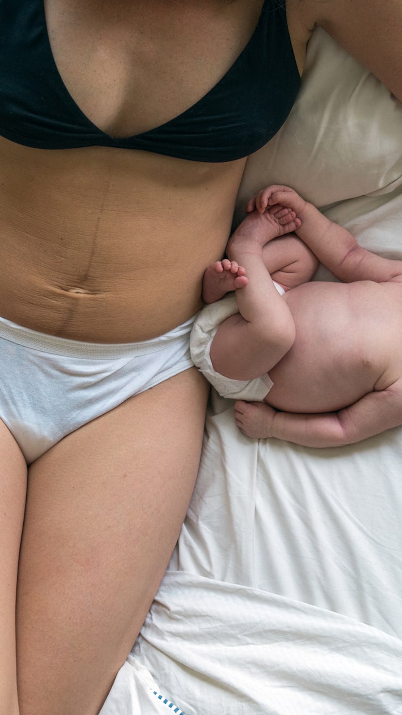 A mom in underwear lying in bed with a cup of coffee with her newborn baby after a C-section with a ...
