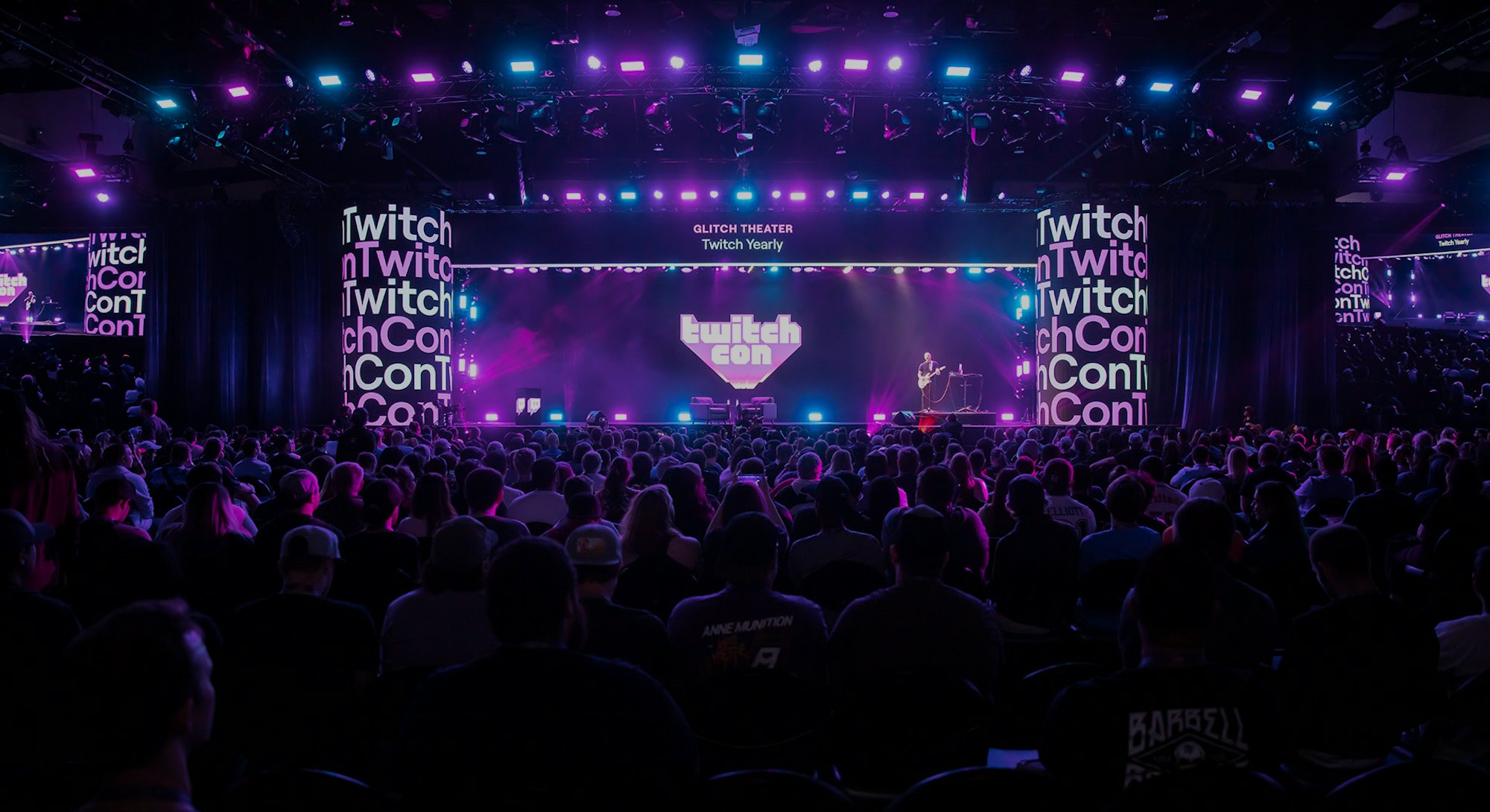 Photo from a past Twitch con showing purple screen with Twitch Con logo and crowd of people seated f...