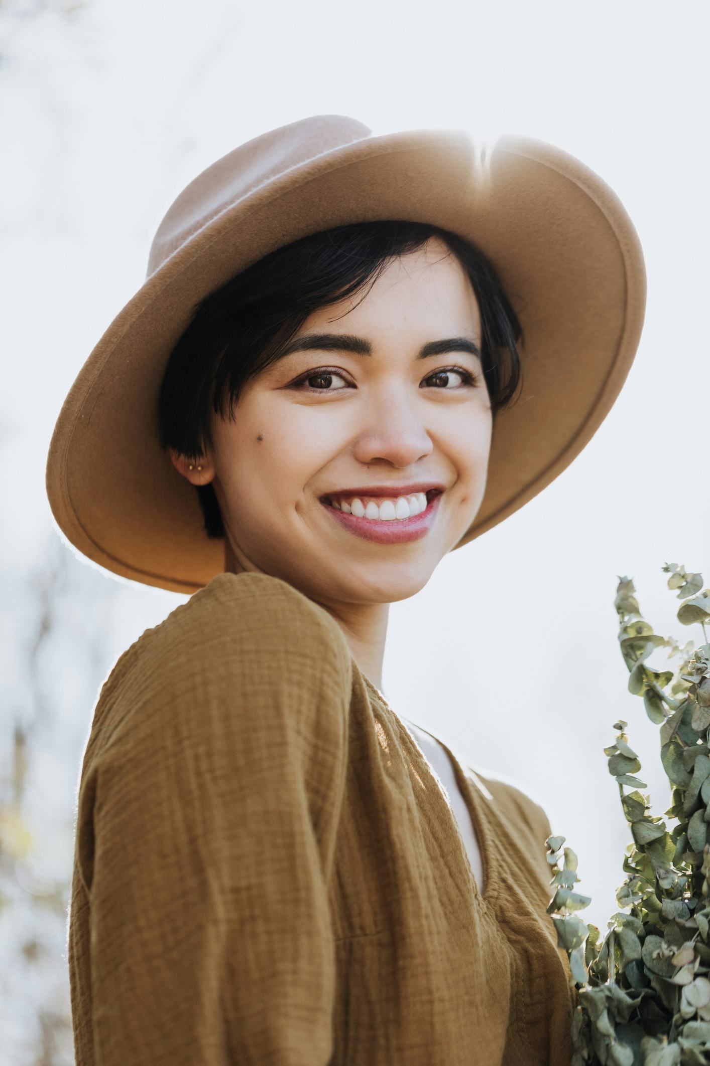 A brunette woman wearing a brown hat and a brown top on a sunny day